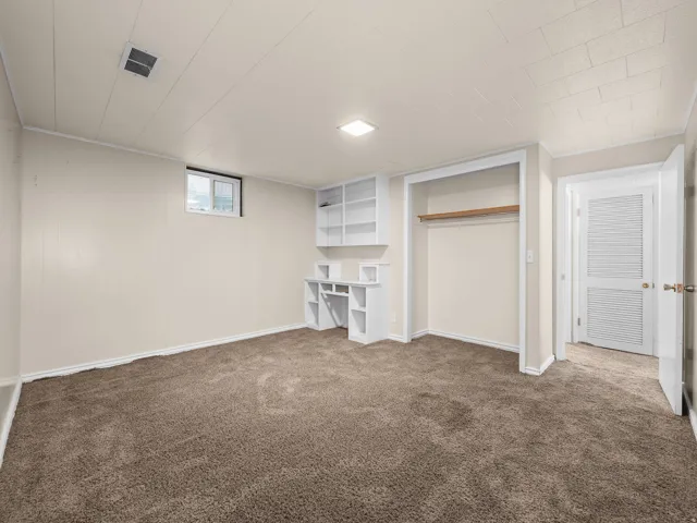 Bedroom 1. Built-in shelving, plush carpeting, built-in desk, and a window