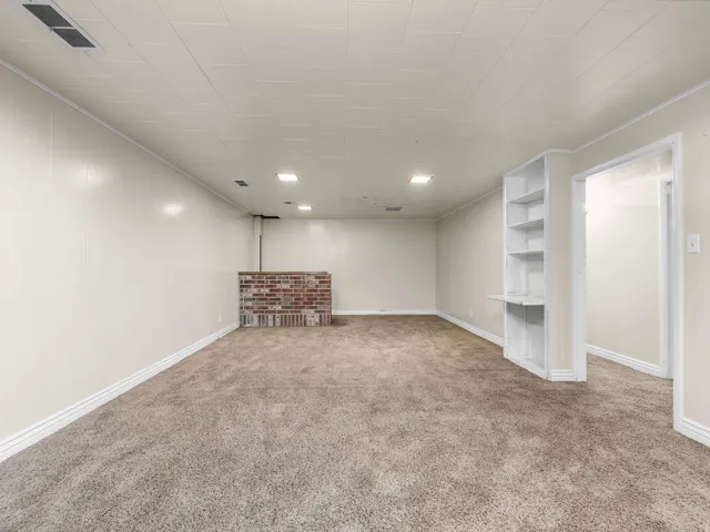 Spacious room featuring neutral carpet, recessed lighting, a built-in shelving unit, and a brick-finish half-wall