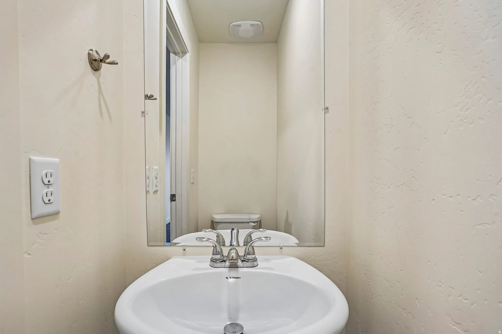 Powder room featuring a pedestal sink with a chrome faucet, a rectangular wall-mounted mirror, and textured light-toned walls