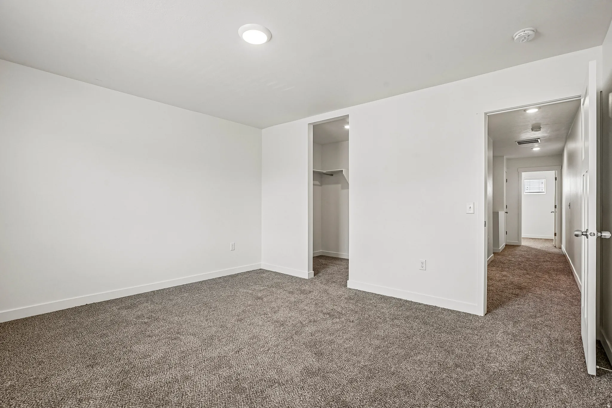 Spacious interior room featuring plush gray carpeting, crisp white walls, recessed ceiling lighting, a built-in closet with shelving, and white trim throughout