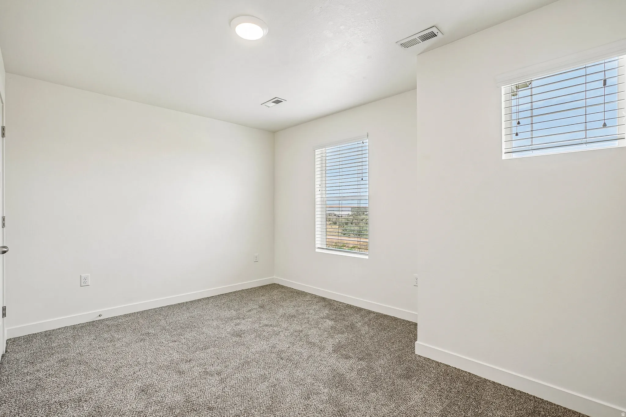 Carpeted room featuring white walls, recessed ceiling lighting, and multiple windows with blinds