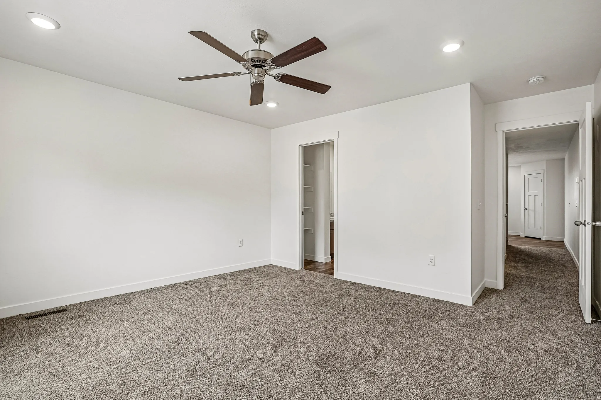 Spacious interior room featuring plush gray carpeting, white walls, recessed lighting, and a ceiling fan with dark wood-finish blades