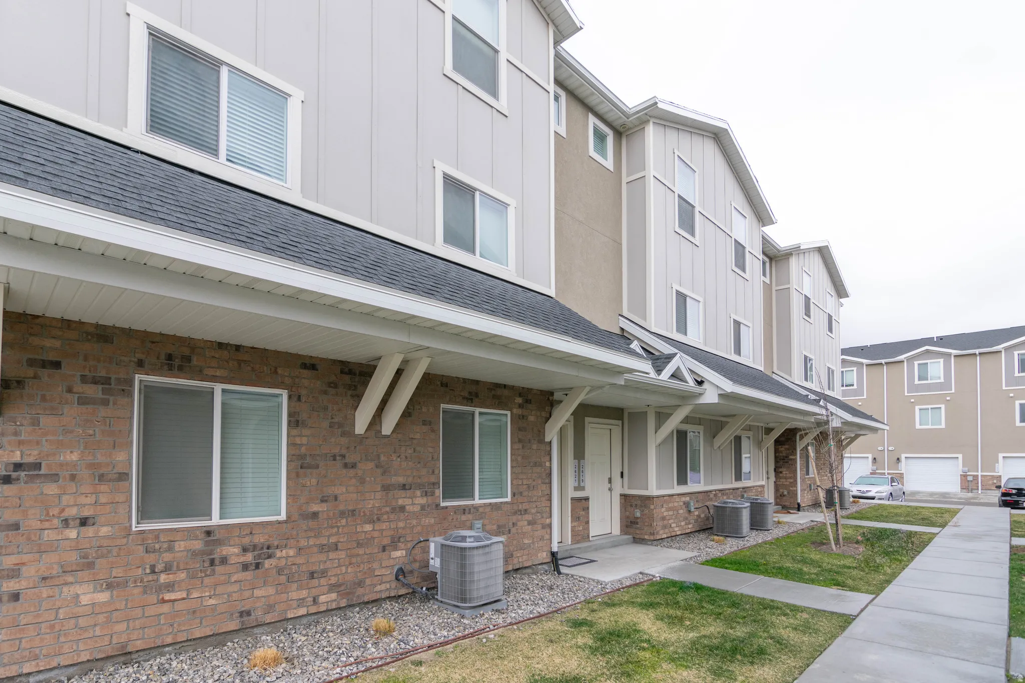 Contemporary townhome-style residences featuring a brick and siding facade, individual entryways, and covered porches