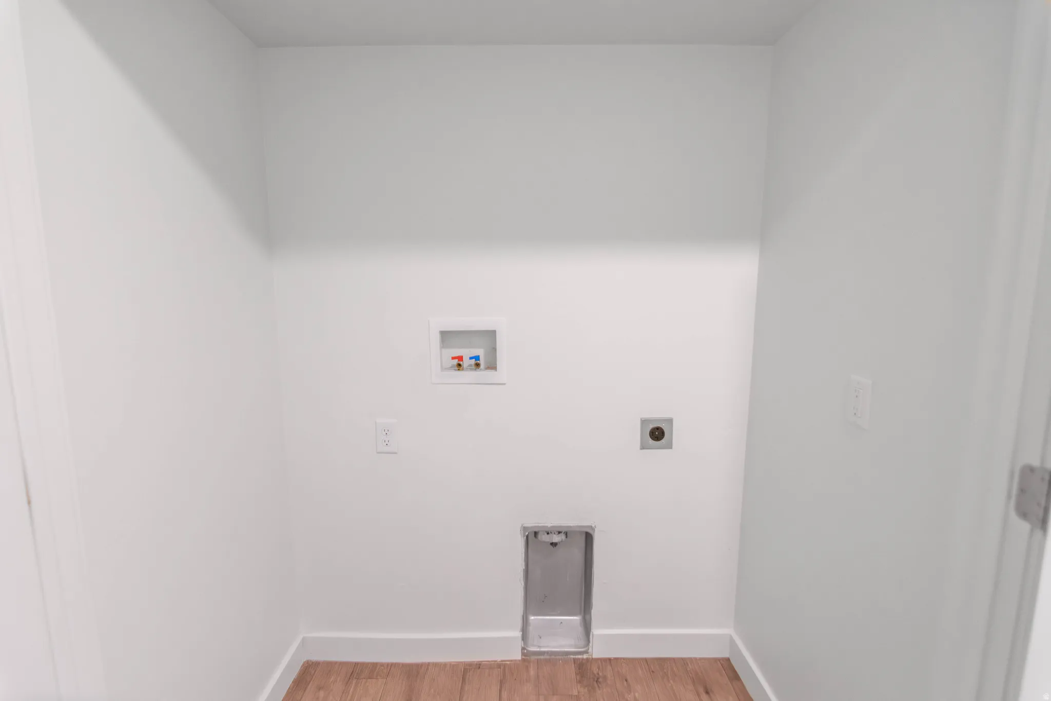 Dedicated laundry area featuring wood-finish flooring, white walls, and essential utility connections