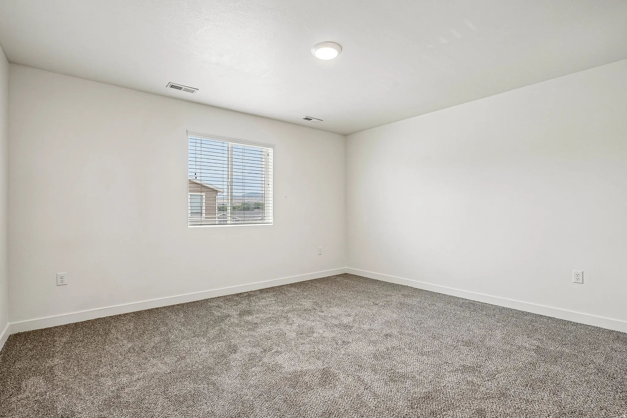 Spacious room featuring neutral carpeting, white walls, and a single window with horizontal blinds