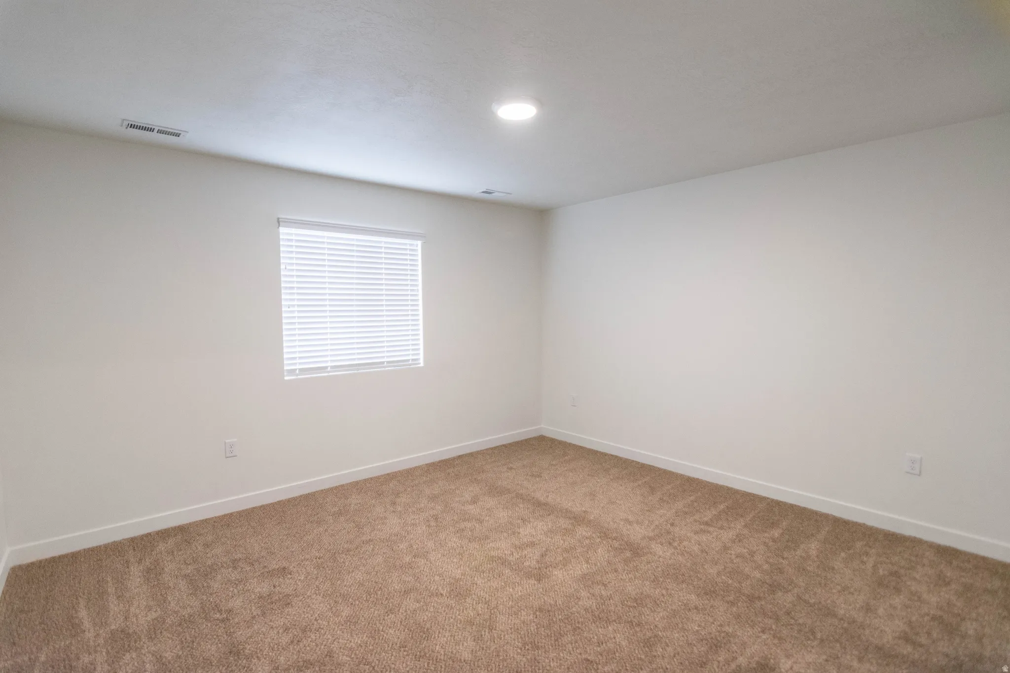 Carpeted room featuring a single window with horizontal blinds, white walls, and a recessed ceiling light