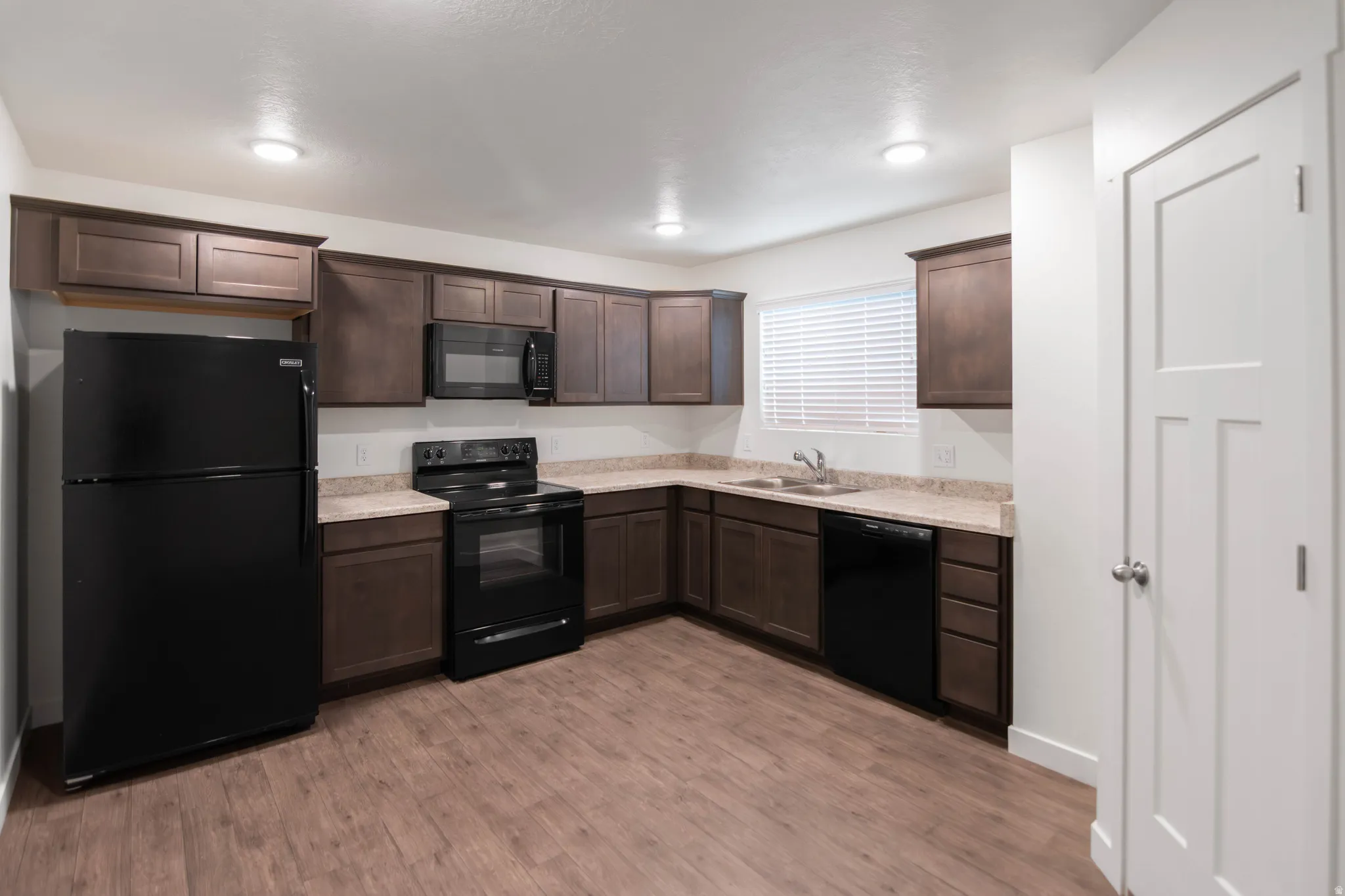 Kitchen featuring wood-finish flooring, dark wood cabinetry, light-toned countertops, and a window with blinds
