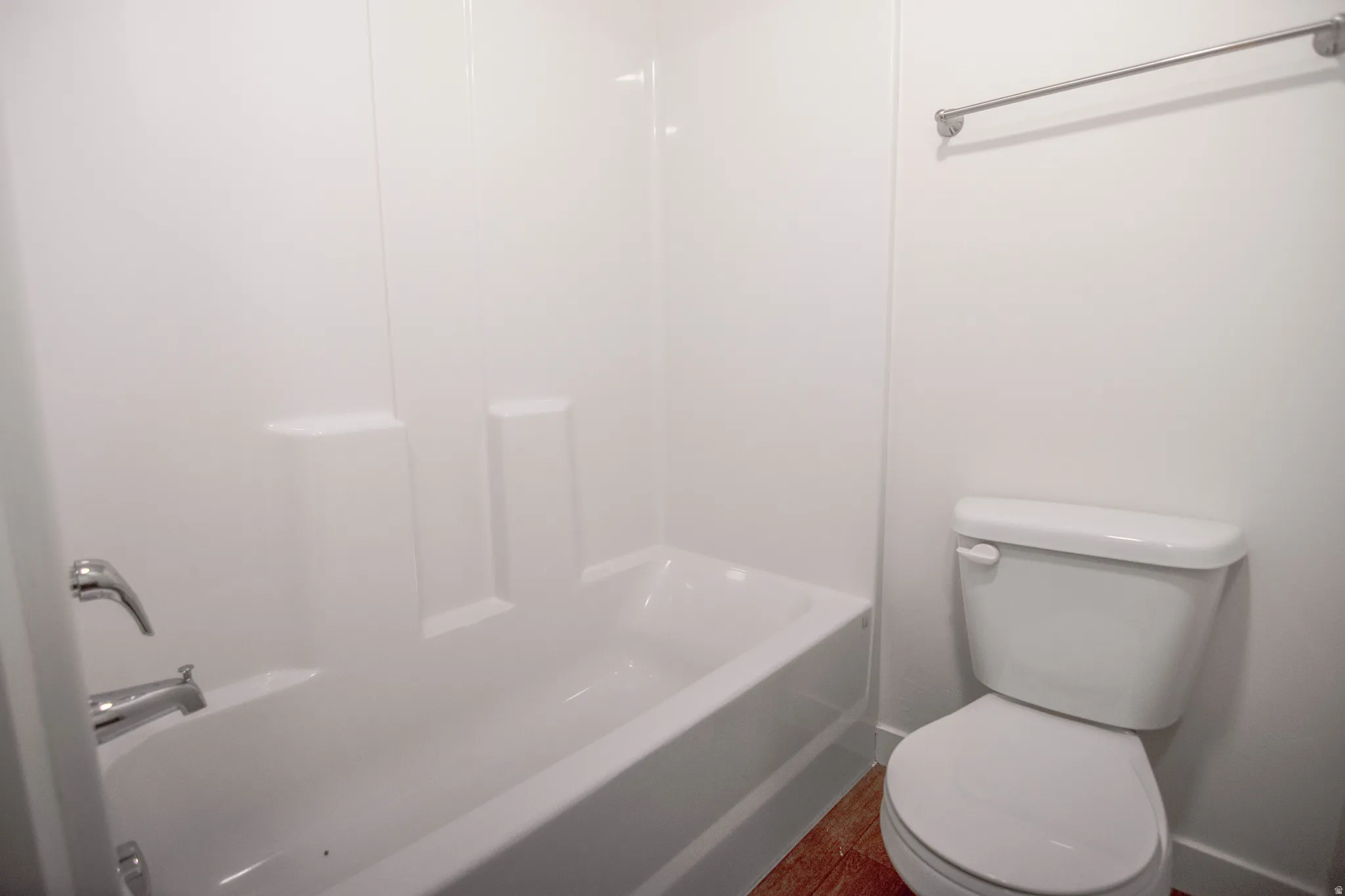 White bathtub and shower surround with chrome fixtures, complemented by a white toilet and wood-finish flooring