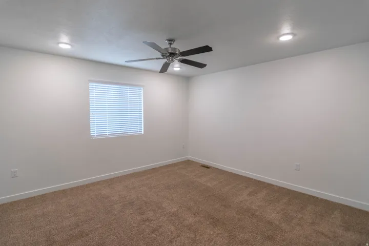 Spacious room featuring neutral carpet flooring, a ceiling fan with light fixture, and recessed lighting