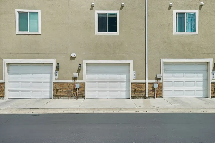 Multi-story building facade featuring three garage doors with paneled designs and exterior sconce lighting