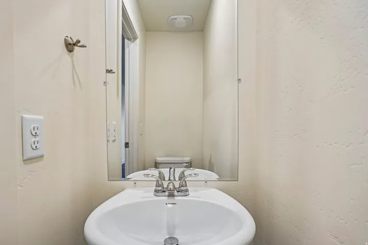 Powder room featuring a pedestal sink with a chrome faucet, a rectangular wall-mounted mirror, and textured light-toned walls