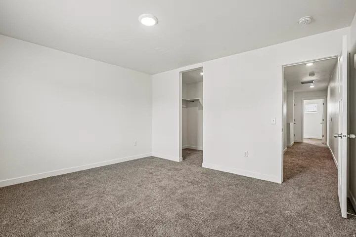 Spacious interior room featuring plush gray carpeting, crisp white walls, recessed ceiling lighting, a built-in closet with shelving, and white trim throughout
