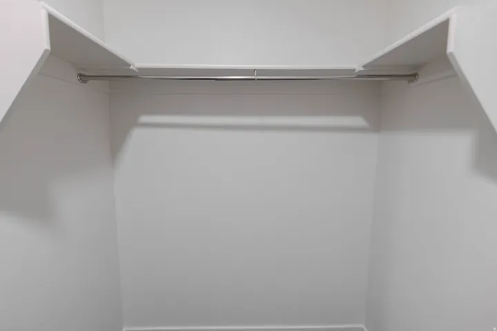 White-painted closet interior with an integrated upper shelf and a chrome hanging rod