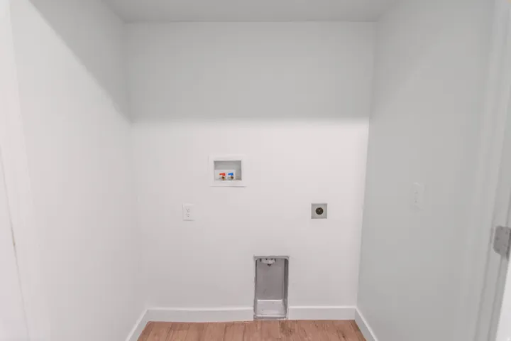 Dedicated laundry area featuring wood-finish flooring, white walls, and essential utility connections