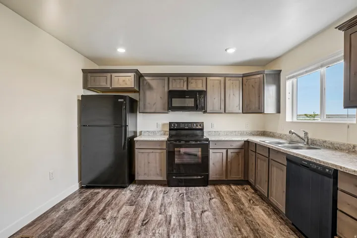 Functional kitchen with wood-finish flooring, light-toned cabinetry, and a full suite of black appliances