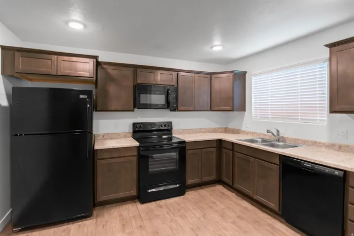 Kitchen featuring wood-finish flooring, dark wood cabinetry, light-toned countertops, and a full suite of black appliances