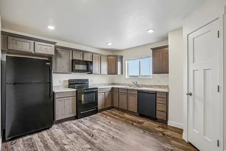 Kitchen featuring wood-finish flooring, two-tone cabinetry, light-toned countertops, and black appliances