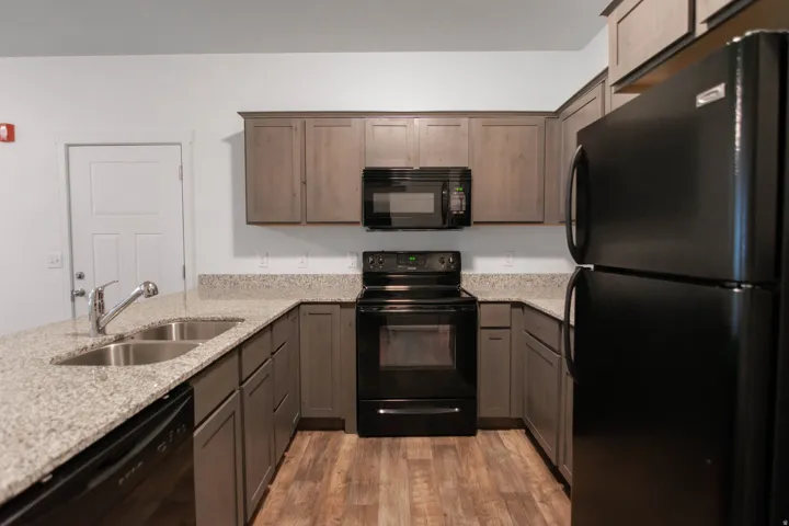 U-shaped kitchen featuring grey cabinetry, speckled countertops, black appliances, and wood-finish flooring