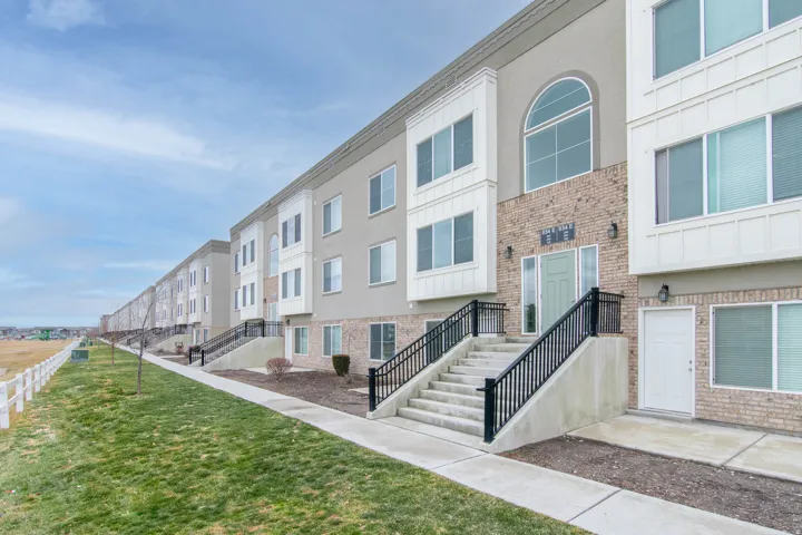 Contemporary townhome exterior featuring a light stucco finish, brick accents, white trim details, an arched second-story window, and a light green entry door with sidelights