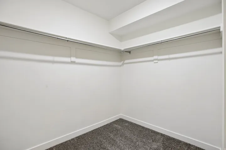 Spacious closet featuring two levels of hanging rods, bright white walls, and dark gray carpet flooring