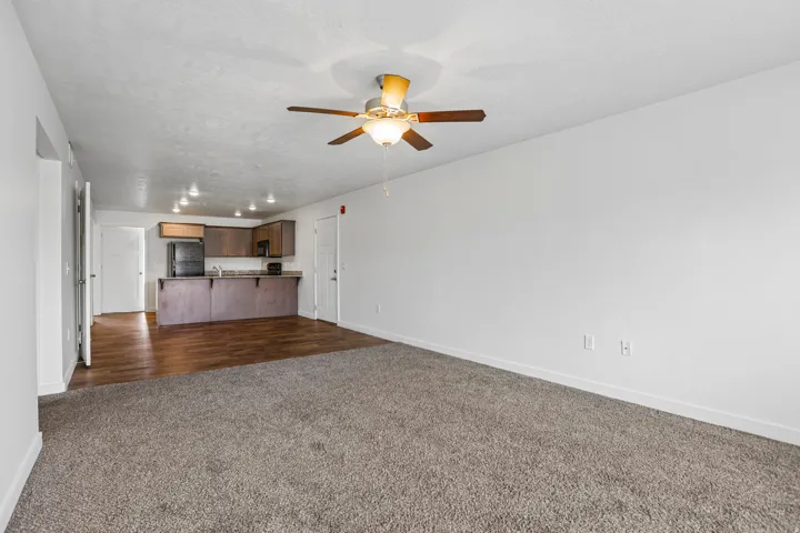 Open-concept living space featuring neutral tone carpeting and a ceiling fan with integrated lighting