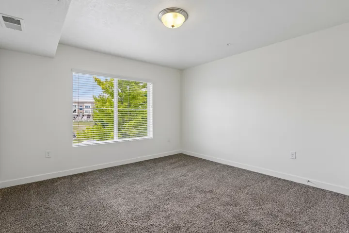 Bedroom featuring a large window with horizontal blinds, neutral-toned carpet, and a flush-mount ceiling light fixture