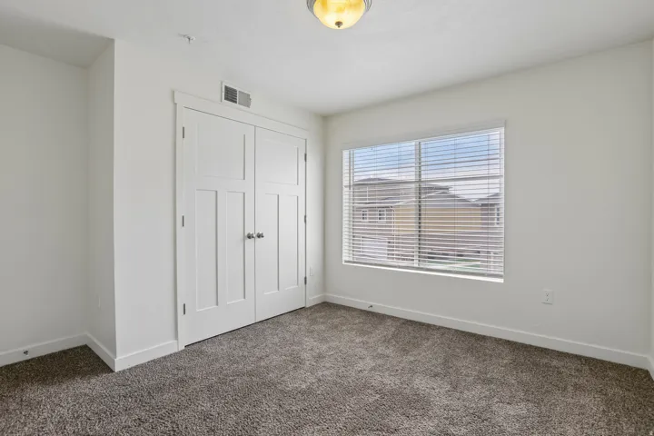 Carpeted room featuring a double-door closet with panel detailing, a single window with blinds, and a flush-mount ceiling light fixture
