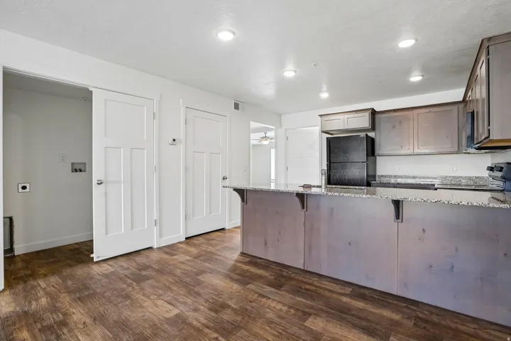 Spacious kitchen featuring a large island with a stone-finish countertop, wood-finish flooring, recessed lighting, and a black refrigerator