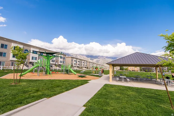 Community green space featuring a shaded pavilion with picnic tables, a playground with slides and climbing structures, and expansive manicured lawns
