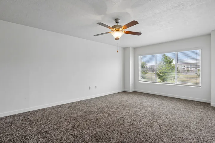 Spacious interior room featuring plush carpet flooring, a multi-pane window with horizontal blinds, and a ceiling fan with integrated lighting
