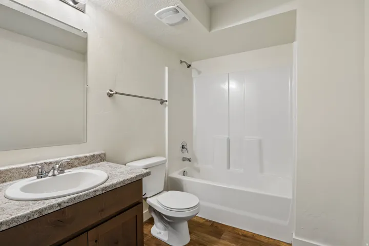Bathroom featuring a white bathtub and shower surround, wood-finish flooring, a toilet, a vanity with a white oval sink, and a mirrored medicine cabinet