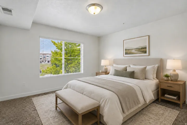 Carpeted bedroom with a large window featuring horizontal blinds