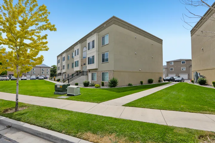 Multi-story townhome with stucco and brick facade, featuring individual entryways and a manicured lawn