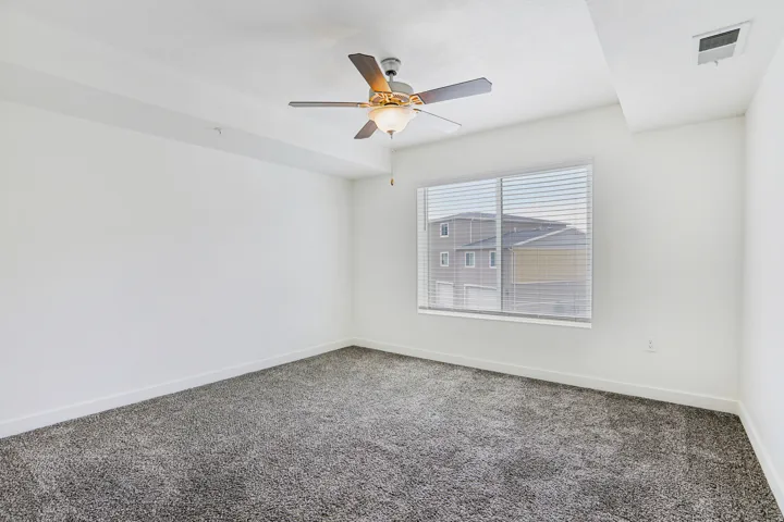 Room featuring light gray carpeting, a large window with white blinds, a ceiling fan with light fixture, and white wall finishes