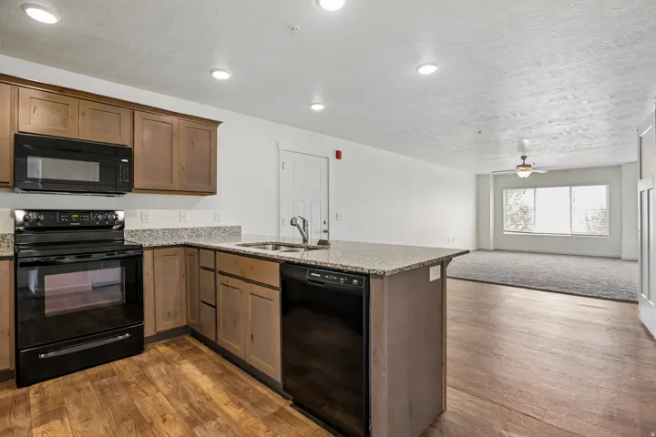 Kitchen featuring wood-finish cabinetry, black appliances, stone-finish countertops, and an integrated sink with a gooseneck faucet
