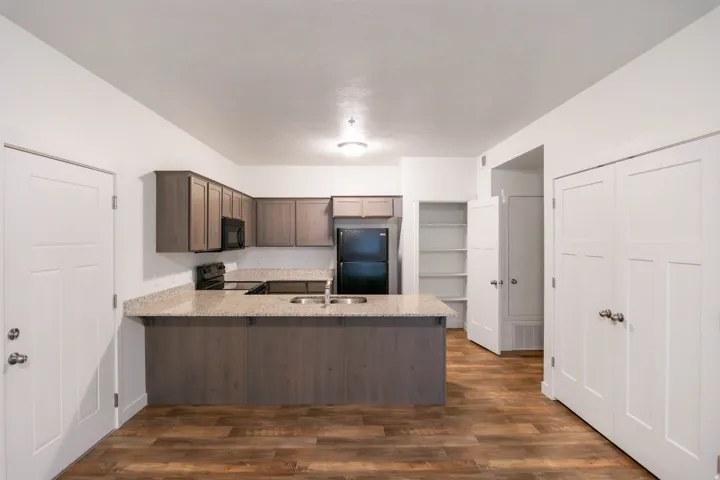 Open-concept kitchen featuring wood-finish flooring, light-colored countertops, dark-toned cabinetry, and stainless steel appliances