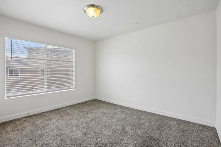 Carpeted room featuring a large window with blinds, white walls, white trim, and a ceiling-mounted light fixture