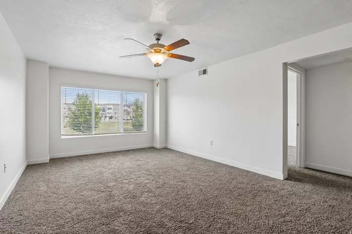 Spacious room featuring neutral carpeting, a large window with horizontal blinds, and a ceiling fan with integrated lighting