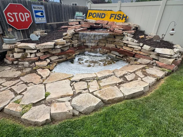 Stone-clad water feature with a waterfall element, surrounded by flagstone paving and a manicured lawn