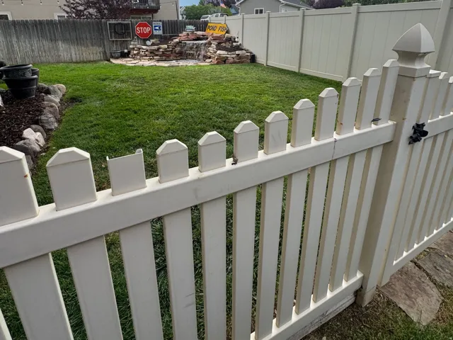 Expansive backyard featuring a manicured lawn, a decorative rock formation, and a white picket fence