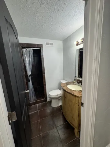 Bathroom featuring a curved vanity with integrated sink, stone countertop, tiled flooring, and a walk-in shower with dark tile surround