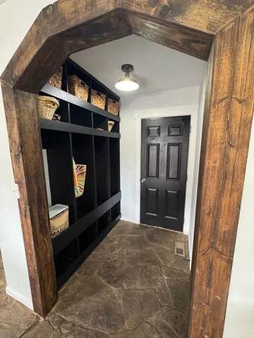 Wood-finish arched entryway framing a mudroom with built-in black shelving