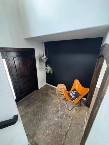 Dark wood-finish entry door with paneling, flagstone-style flooring, and a dark accent wall
