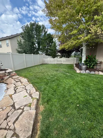 Expansive backyard featuring a lush lawn, a stone-edged garden bed, mature trees, and a combination of privacy and picket fencing