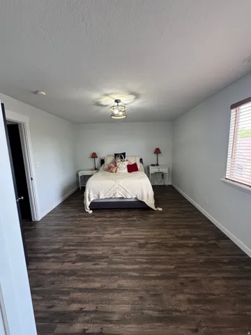 Spacious room featuring wood-finish flooring, a contemporary ceiling light fixture, and a window with blinds
