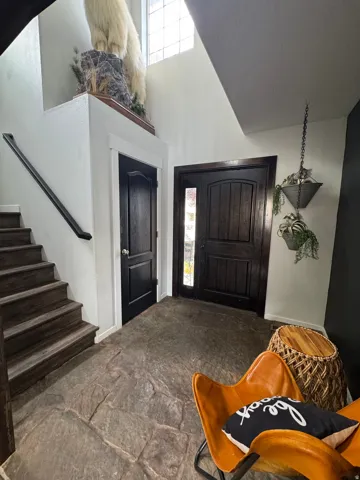 Foyer with natural stone flooring, dark wood entry door with glass light, and a dark wood staircase with a black handrail