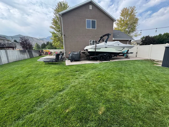 Expansive backyard featuring a manicured lawn, concrete patio, and a privacy fence