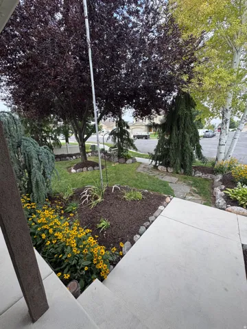 Manicured front yard with mature trees, established landscaping, and a stone-paved walkway