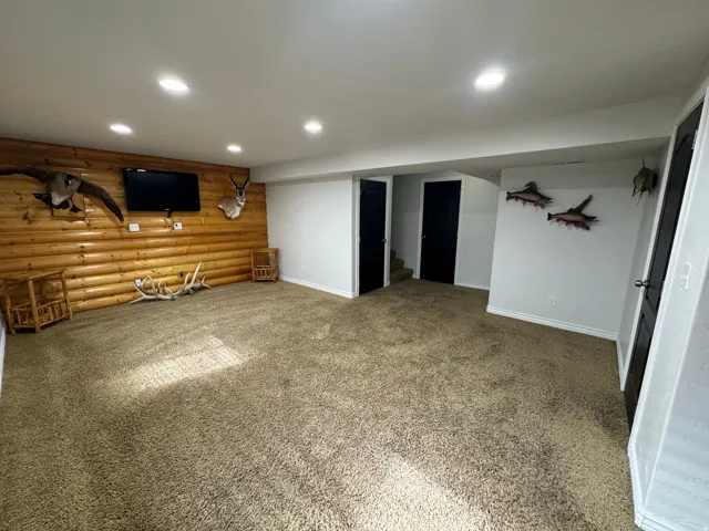 Spacious room featuring a log-style accent wall, recessed lighting, and carpet flooring