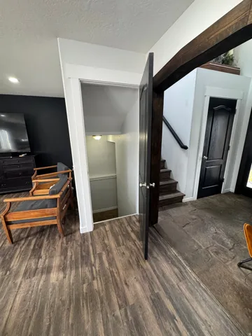 Wood-finish flooring, dark wood-tone accent beam, white trim, and a dark paneled door